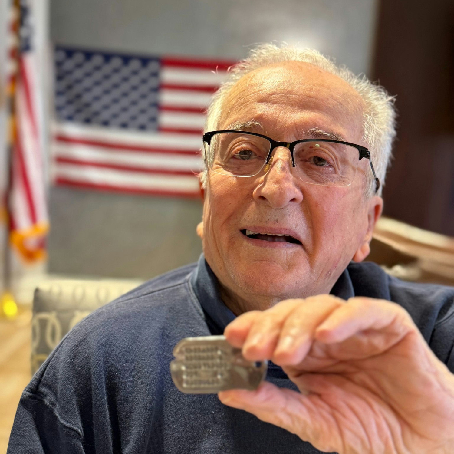 A resident at Arbor Terrace Norwood smiles while holding a small keepsake near an American flag, sharing a meaningful moment at this senior living community serving Bergen County.