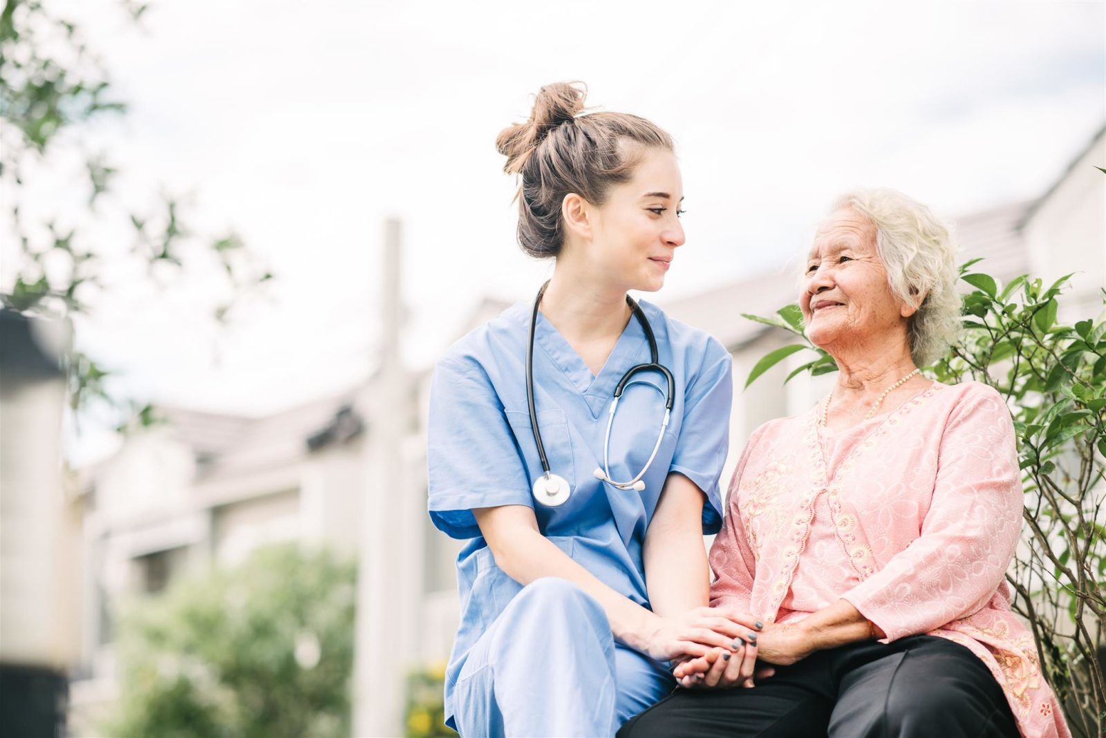 a senior woman and a nurse sitting down and holding hands