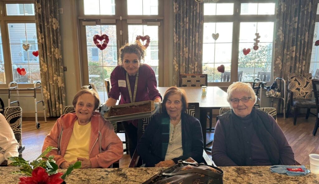 Three of SLR Marlboro's assisted living resident's sitting at a countertop with an associate standing behind them