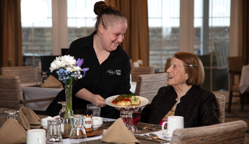 An associate serving an assisted living resident dinner at SLR Marlboro.