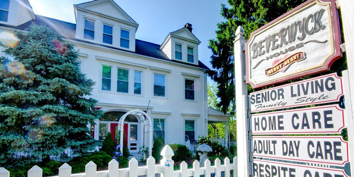 A charming senior living home with a white picket fence and bright blue sky.