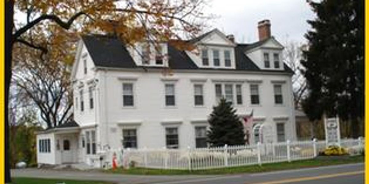 Large white colonial-style house with a picket fence and autumn trees.