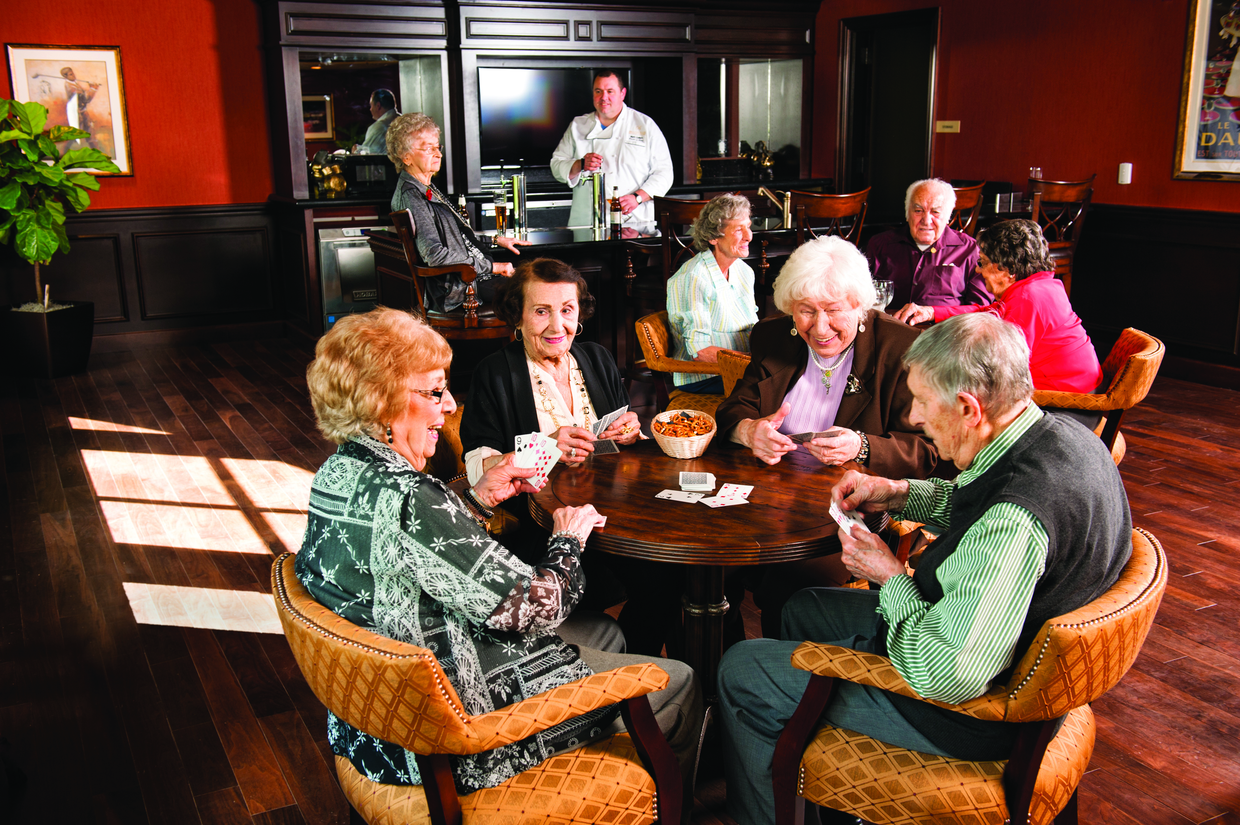 several residents sitting around a table with a bar and bartender in the background