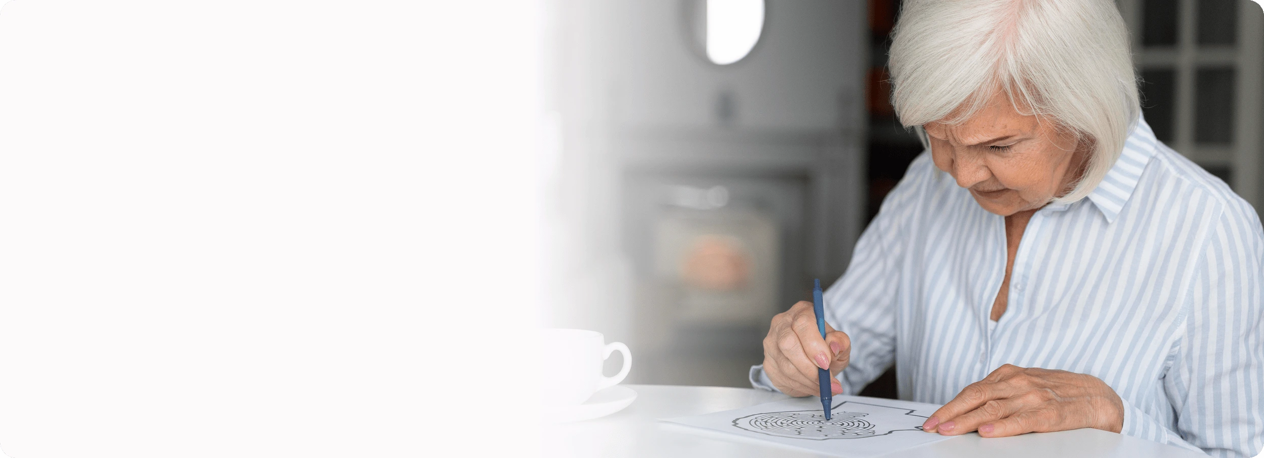 A senior woman with short white hair looks down intently, writing or drawing with a pen.